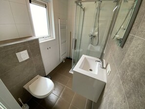 Een badkamer met toilet, wastafel, douchecabine van glas en een raam.