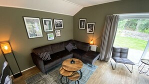 A modern living room with a sectional sofa, a round coffee table, a side table, a chair, and a large window with curtains. - Holiday Home in Maarn With Terrace (Maarn)