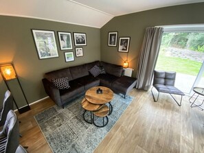 Een moderne woonkamer met een modulaire bank, een ronde salontafel, een bijzettafeltje, een stoel en een groot raam met gordijnen.