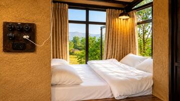 A bedroom with a large window, a bed with white bedding, and a wall-mounted electrical panel.