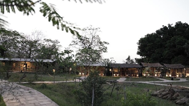 A series of rustic cabins with thatched roofs, surrounded by lush greenery and a stone pathway.