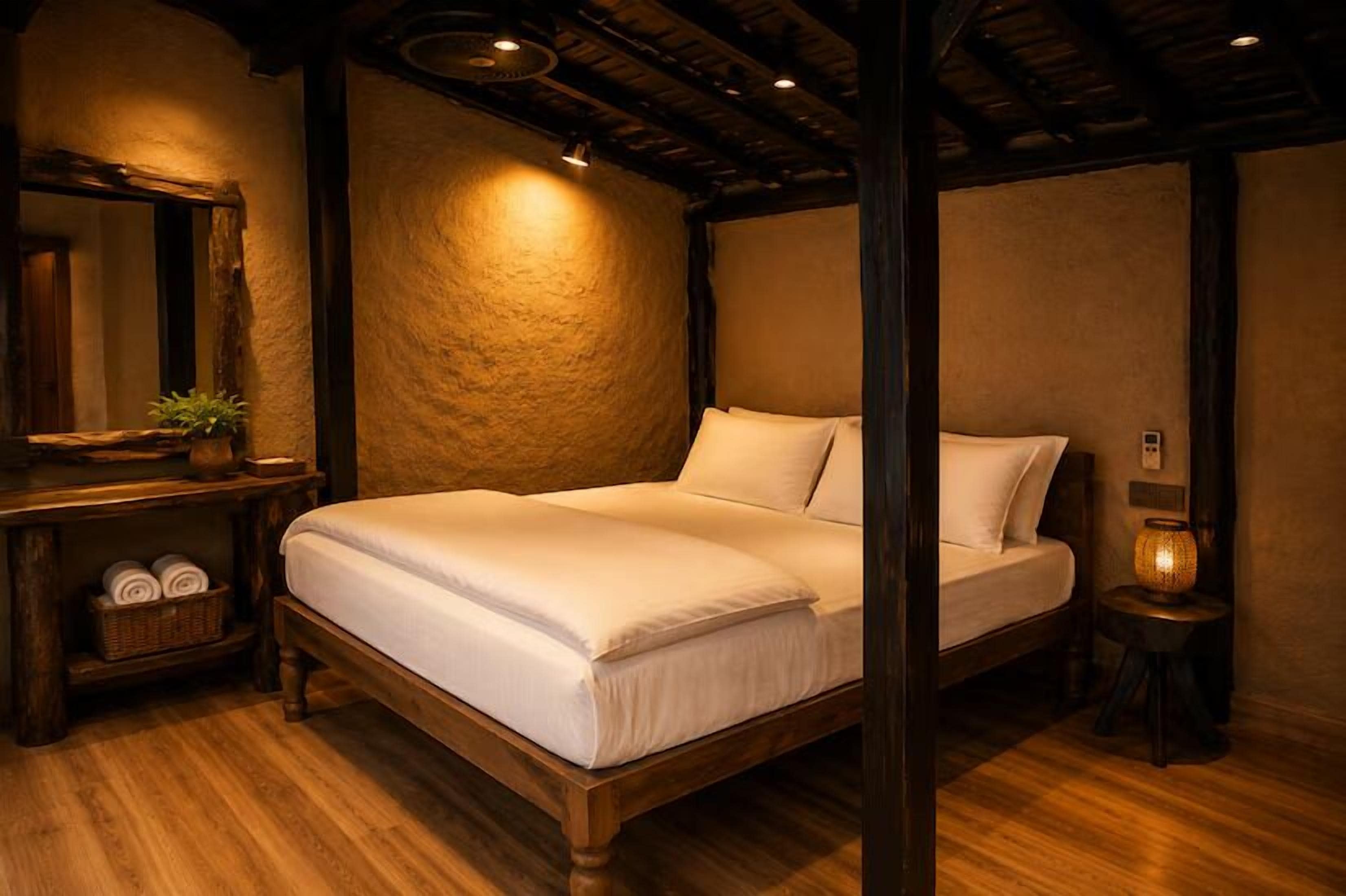 Uma cama de madeira com roupa de cama branca num quarto com parede texturizada e chão de madeira.
