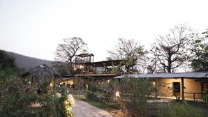 A two-story building with a stone pathway leading to it, surrounded by vegetation.