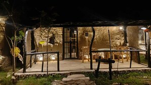 An outdoor dining area with stone walls, a covered seating area, and a pathway leading to the entrance.