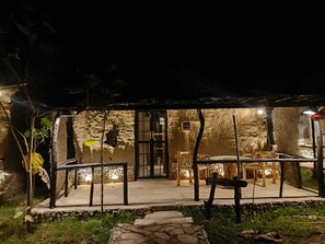 An outdoor dining area with stone walls, a covered seating area, and a pathway leading to the entrance. - Bhuvan Aarogyam Vanvaasi  (Rajnagar)