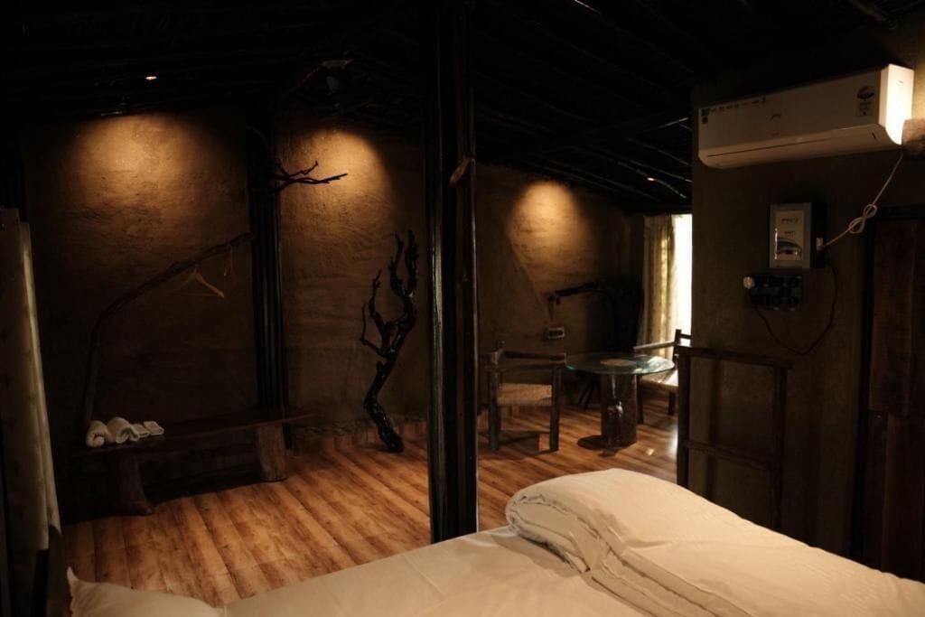 A dimly lit room with a bed, a wooden bench with shoes, a small table, and a chair.