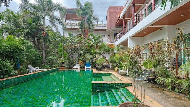 A swimming pool with a green tile surface, surrounded by lush greenery and a multi-level building with balconies. - Relaxing 1BR Close to Beach & Lake- relife C200 (Tambon Rawai)