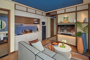 Quarto de hotel moderno com cozinha compacta, sofá, mesa de centro e estante de livros.