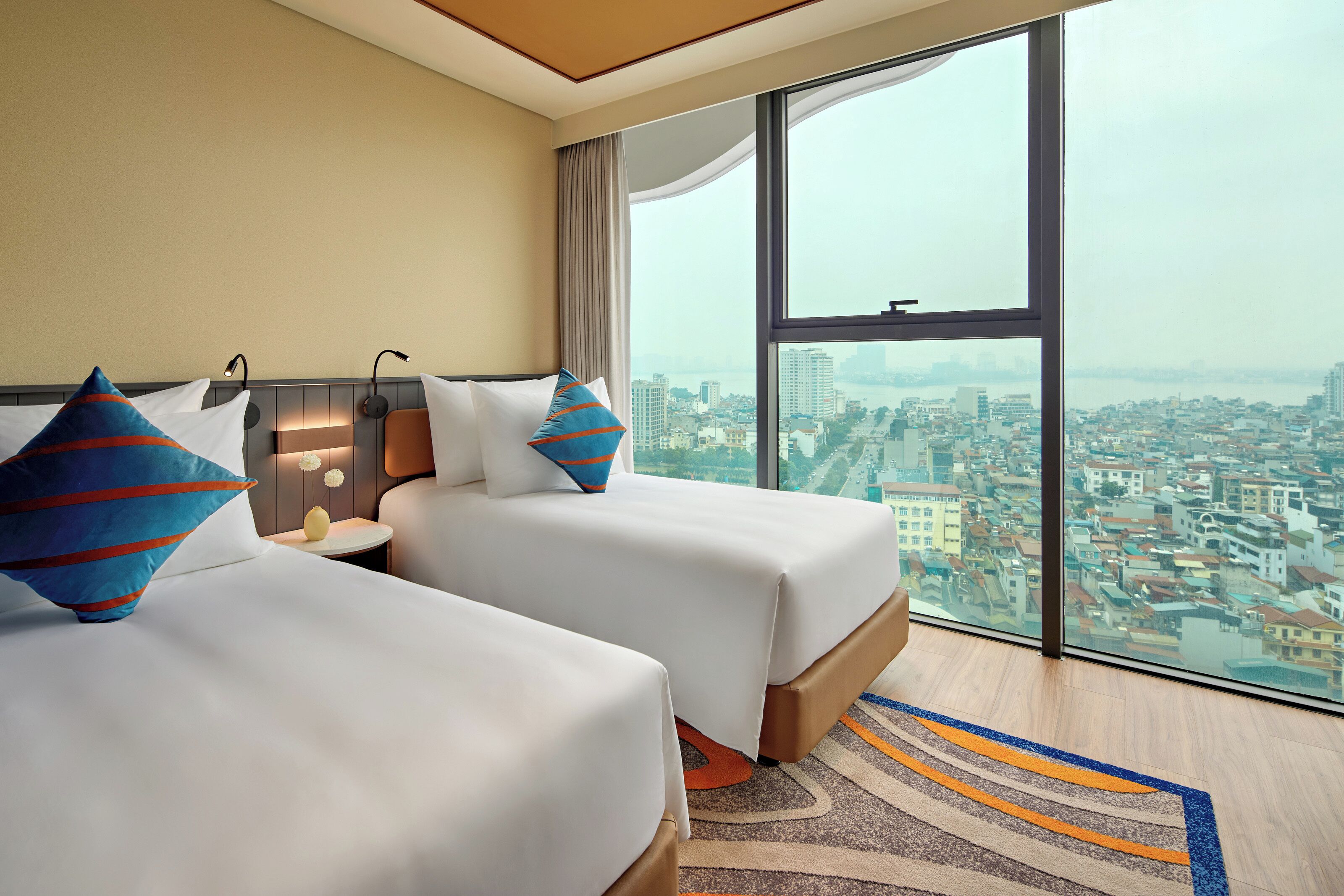 Quarto de hotel com duas camas, uma janela grande e vista para a paisagem urbana.