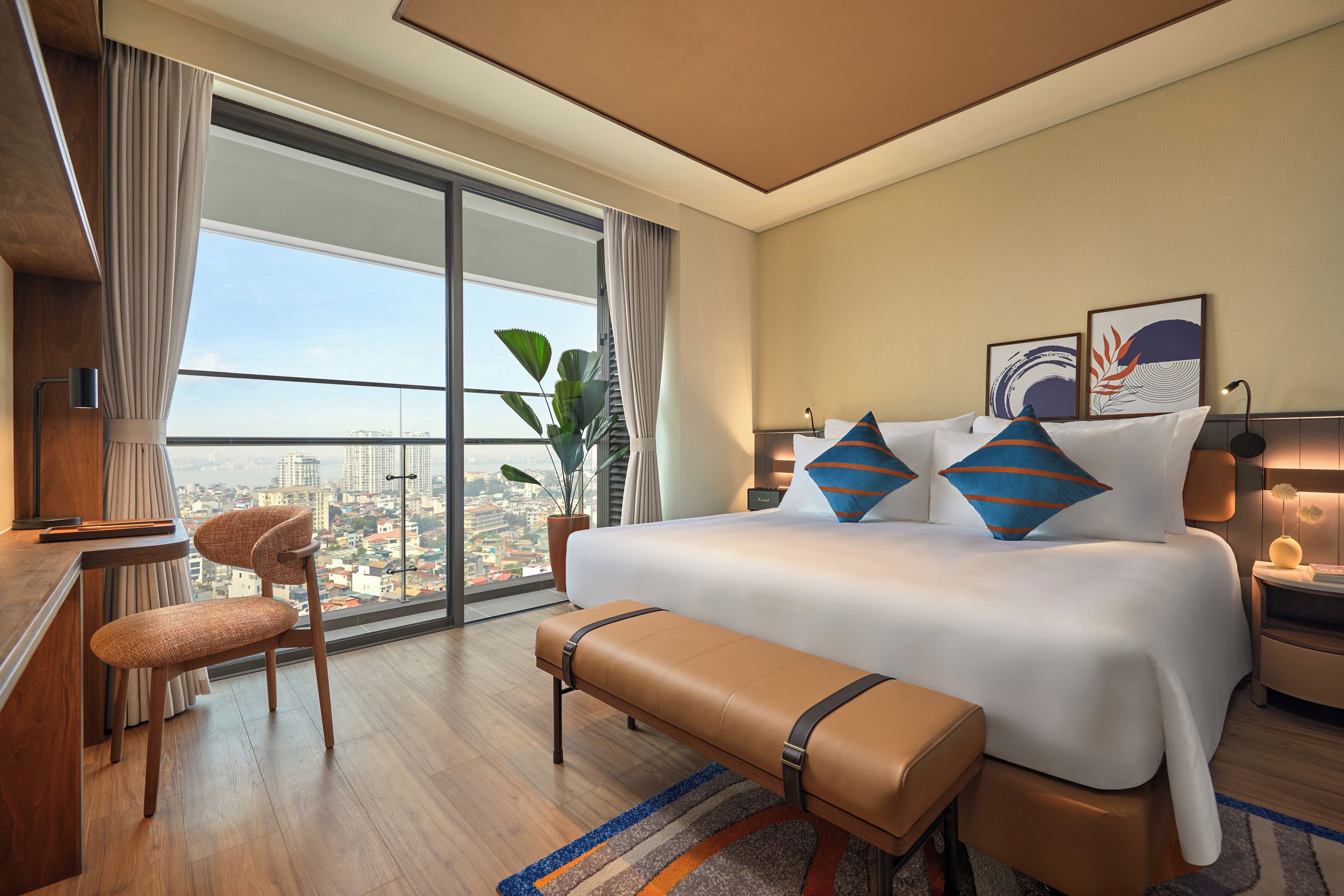 Quarto de hotel com uma cama grande, uma escrivaninha, uma cadeira, um banco e vista para a cidade.