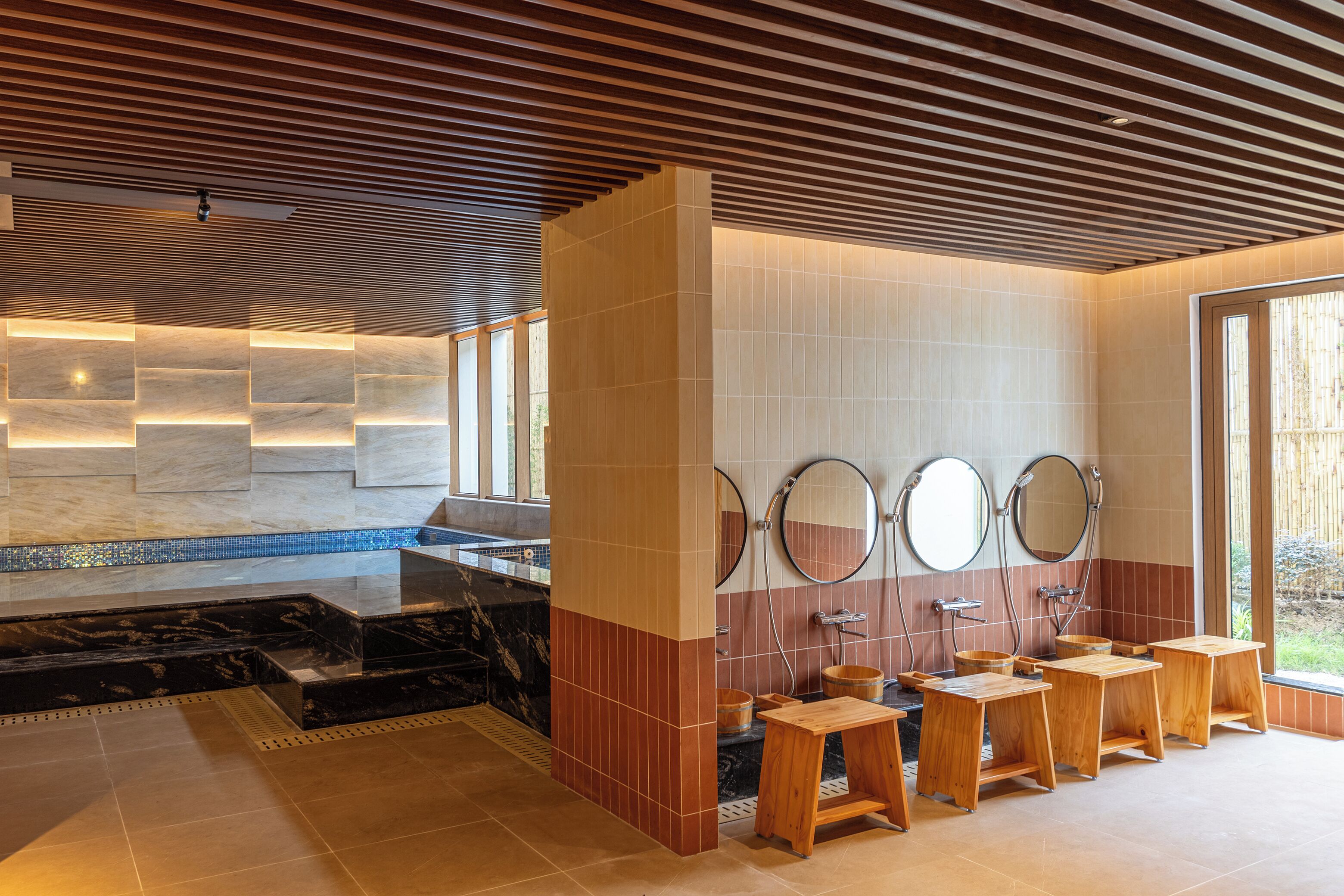 Un baño moderno con lavamanos de mármol, taburetes de madera y un espejo grande.