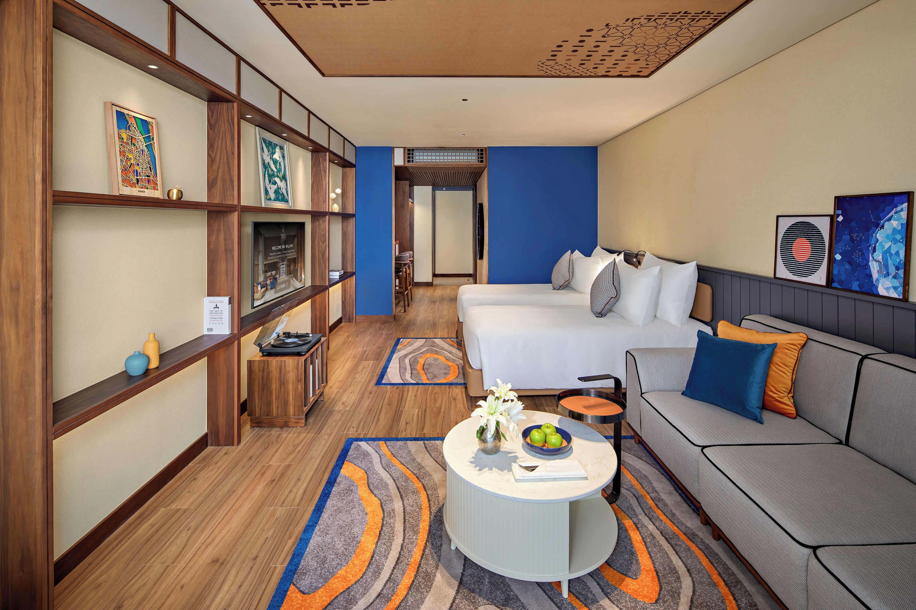 Quarto de hotel com cama, sofá, mesa de centro redonda e obras de arte nas paredes.