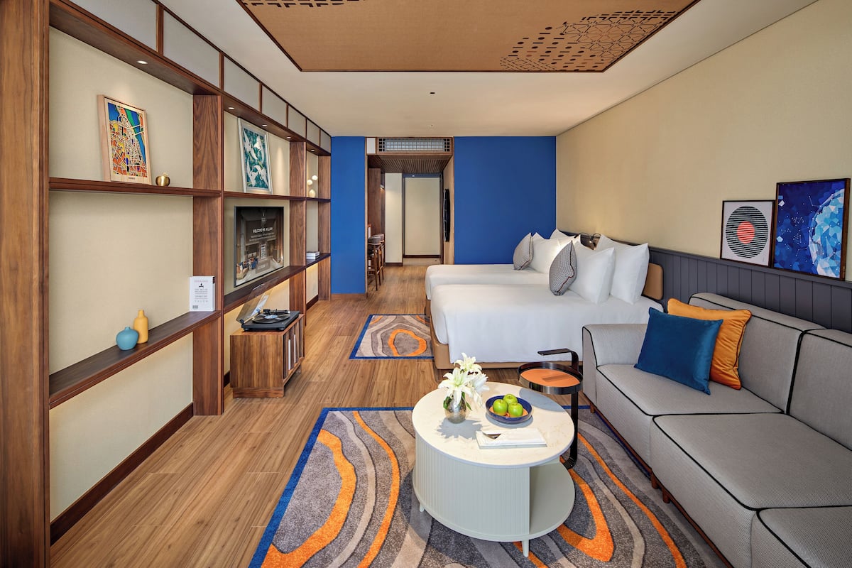 Habitación de hotel con cama, sofá, mesa de centro redonda y obras de arte en las paredes.