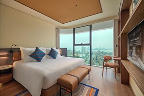 Quarto de hotel moderno com uma cama grande, um banco, uma escrivaninha e vista para a cidade.