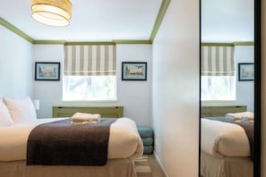 Ein Schlafzimmer mit einem Bett, einem Fenster mit gestreiftem Rollo und zwei gerahmten Bildern an der Wand.