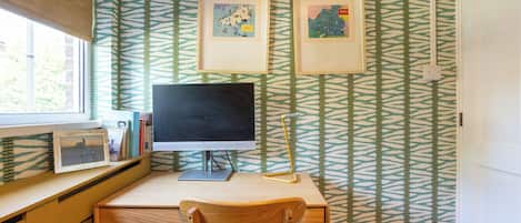 A room with a desk, a computer, and two framed pictures on the wall.
