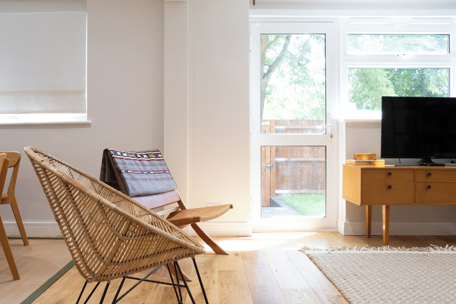 A room with a wicker chair, a television on a wooden cabinet, and a door leading outside.