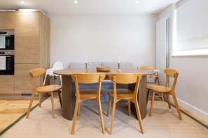 A dining area with a round table and six wooden chairs, a striped sofa, and a white radiator. - Serene Midcentury Modern Family Home in Islington (Greater London)