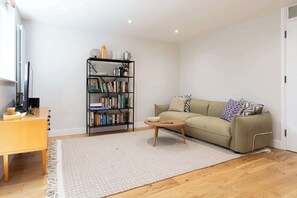 Ein Wohnzimmer mit Sofa, Couchtisch, Bücherregal und Schreibtisch mit Computer.