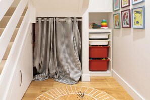 A hallway with a striped curtain, a storage unit with red bins, and a wall with framed artwork. - Serene Midcentury Modern Family Home in Islington (Greater London)