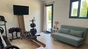 Ein Wohnzimmer mit Sofa, Fernseher, Trainingsgeräten und einem Fenster.
