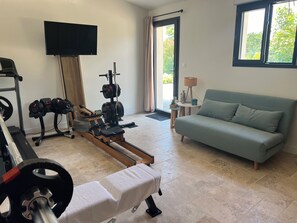 A living room with a sofa, TV, exercise equipment, and a window. - A lovely house with a private pool, in a quiet location, 20 minutes from Lyon (Dardilly)