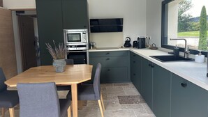 Eine moderne Küche mit integriertem Mikrowellenherd, Backofen und Kaffeemaschine, ein Essbereich mit Holztisch und Stühlen sowie ein Fenster mit Blick ins Grüne.