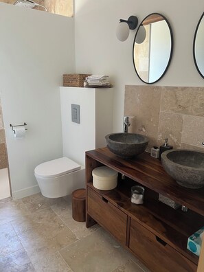 Une salle de bain moderne comprenant des toilettes, un meuble-lavabo avec de grands vasques en pierre, un meuble en bois et un miroir.
