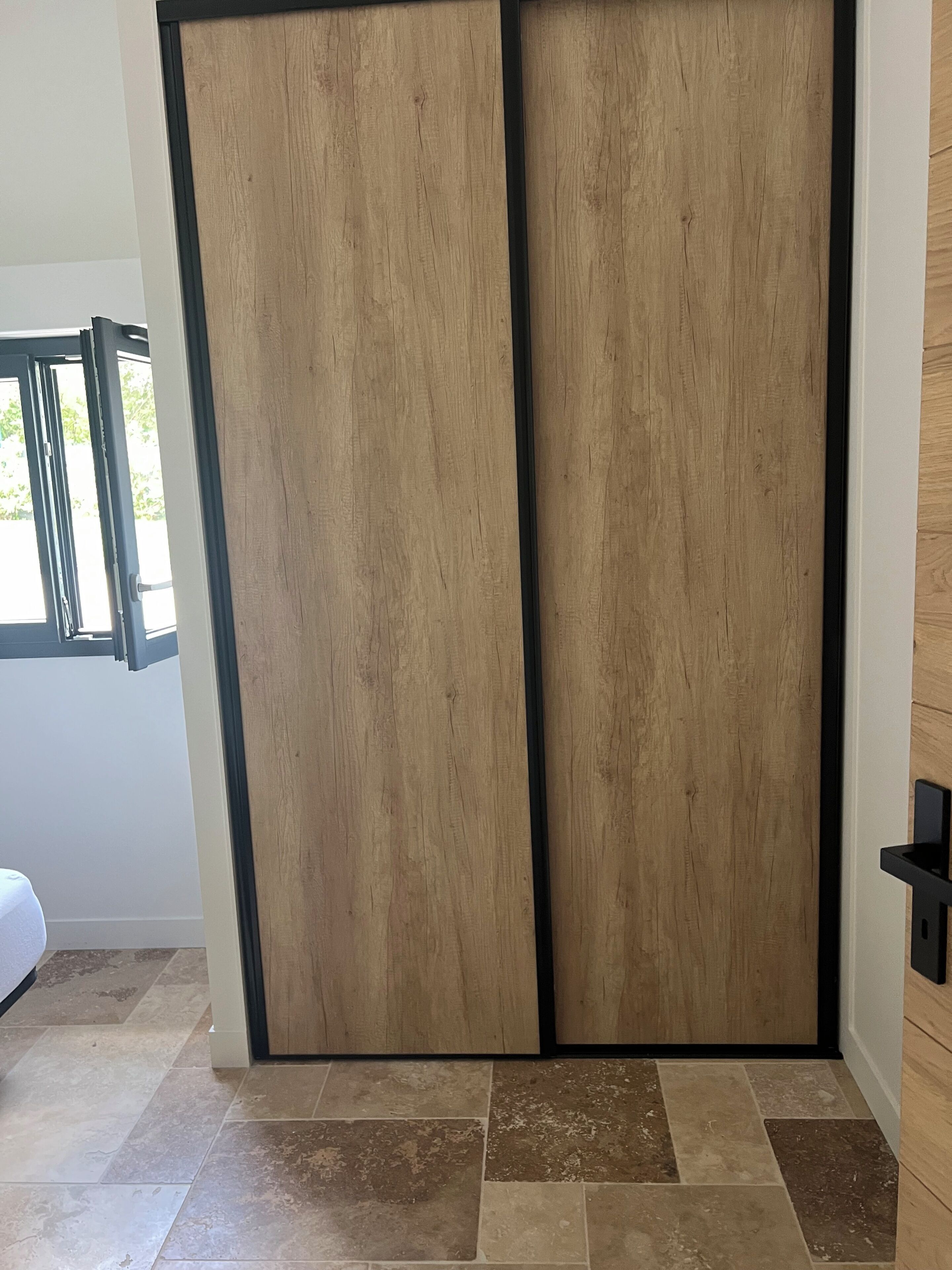 A room with a sliding wooden door, a bed with a white headboard, and a tiled floor.