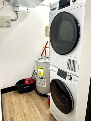 A laundry room with stacked washers and dryers, a water heater, and a red bucket. - Brick & Bed - Beautiful Historic Riverfront Loft (St. Louis)