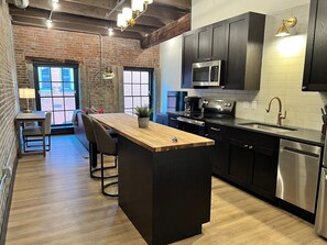 A modern kitchen with a central island, stainless steel appliances, and a brick wall. - Brick & Bed - Beautiful Historic Riverfront Loft (St. Louis)