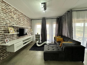 Una sala de estar con pared de ladrillo, televisor de pantalla plana, sofá y comedor con vistas.