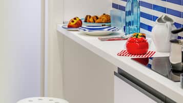 A kitchen with white cabinets, a blue-striped backsplash, two white stools, and various kitchen items on the counter.
