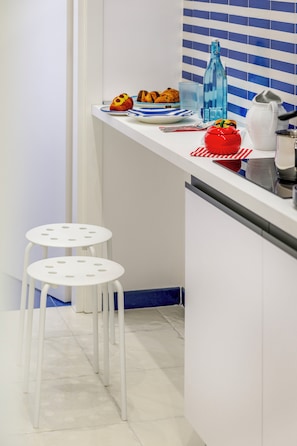 A kitchen with white cabinets, a blue-striped backsplash, two white stools, and various kitchen items on the counter. - Bellamore (Piano di Sorrento)