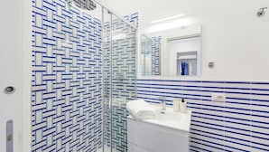 A bathroom with a patterned tile wall, a glass shower enclosure, and a white sink with a mirror above it.