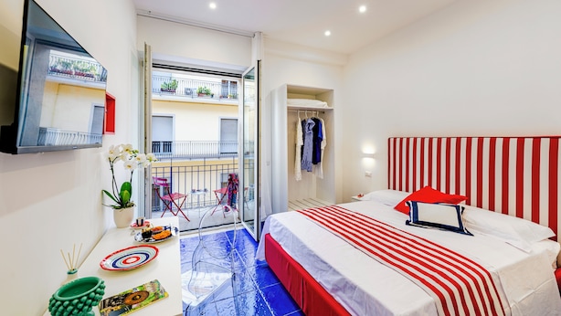A hotel room with a bed, a TV, a balcony with a view of the building, and a dining area with chairs and a table.