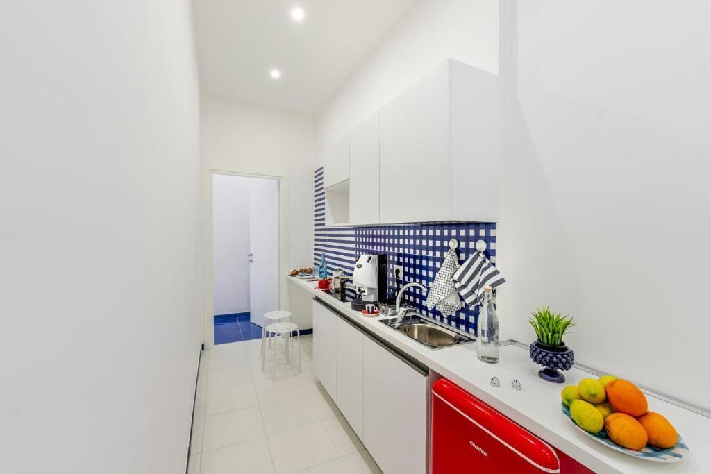A narrow kitchen with white cabinets, a red dishwasher, and a blue tiled backsplash.