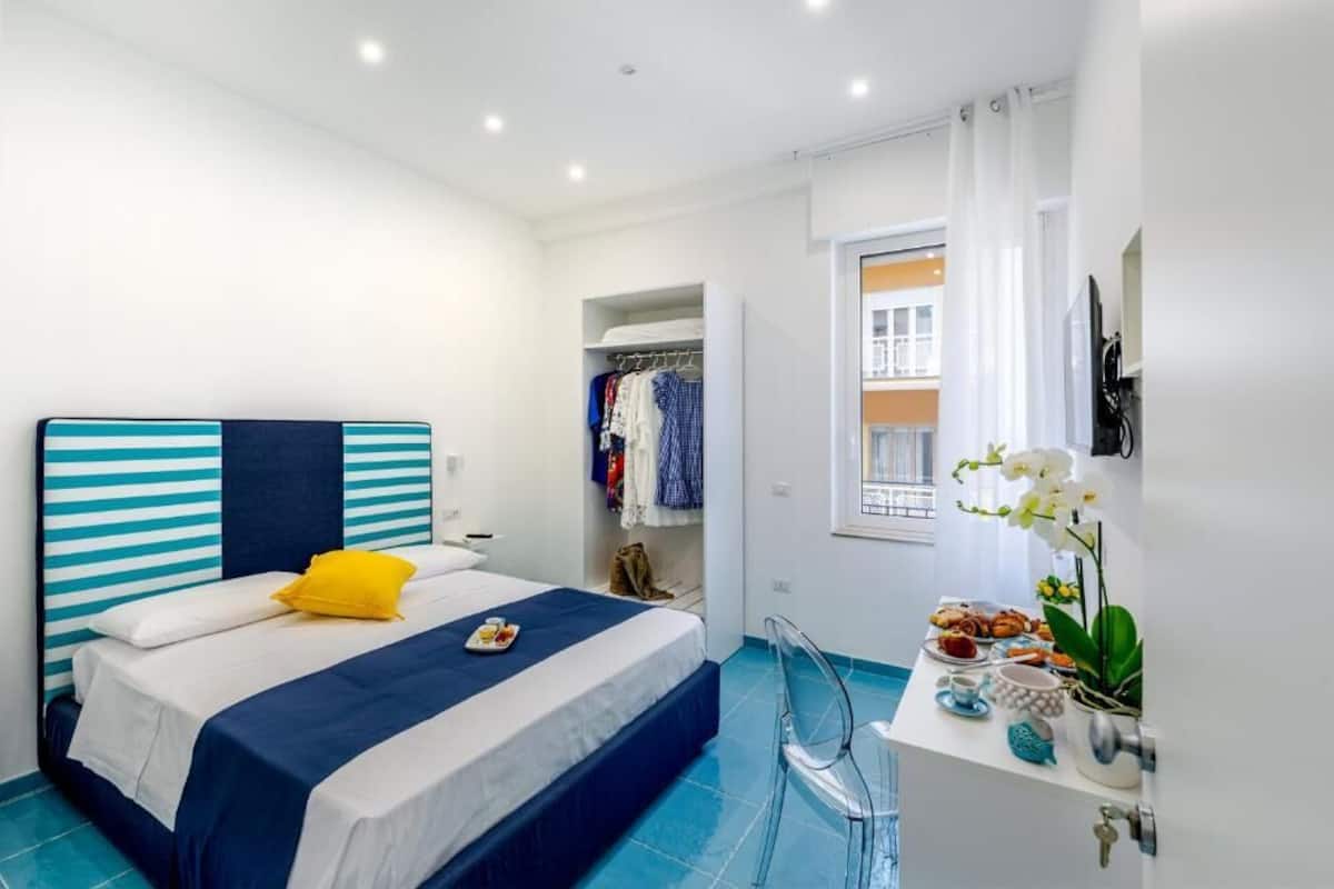 A bedroom with a bed, a desk with a chair, a wardrobe, and a window with curtains.