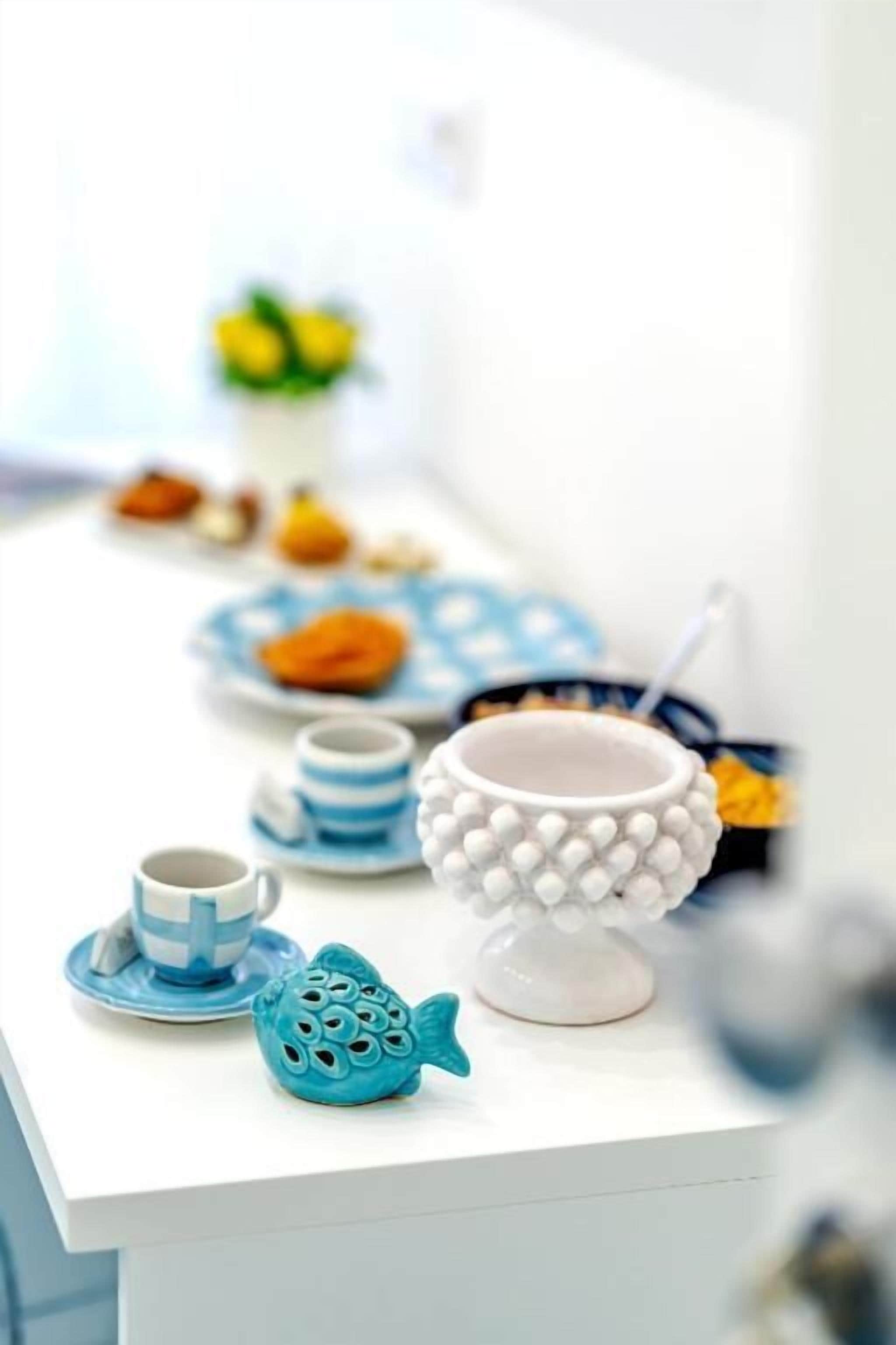 A white table with a blue fish-shaped salt shaker, a white teapot, and a blue and white striped cup.