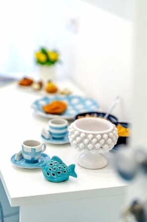 A white table with a blue fish-shaped salt shaker, a white teapot, and a blue and white striped cup. - Bellamore (Piano di Sorrento)