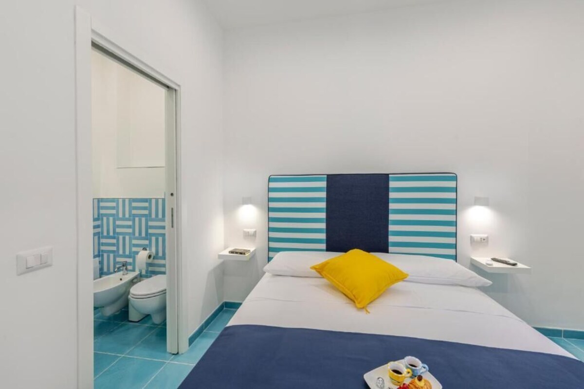 A hotel room with a bed, a nightstand, a bedside table, a bathroom with a toilet and bidet, and a patterned wall.
