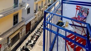 A narrow street with buildings on either side, a blue metal railing, and a chair.