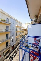 Uma rua estreita com edifícios em ambos os lados, um corrimão de metal azul e uma cadeira.