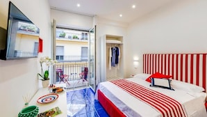 A bedroom with a bed, a small table with a vase and a plate, a mirror, and a balcony with a railing.