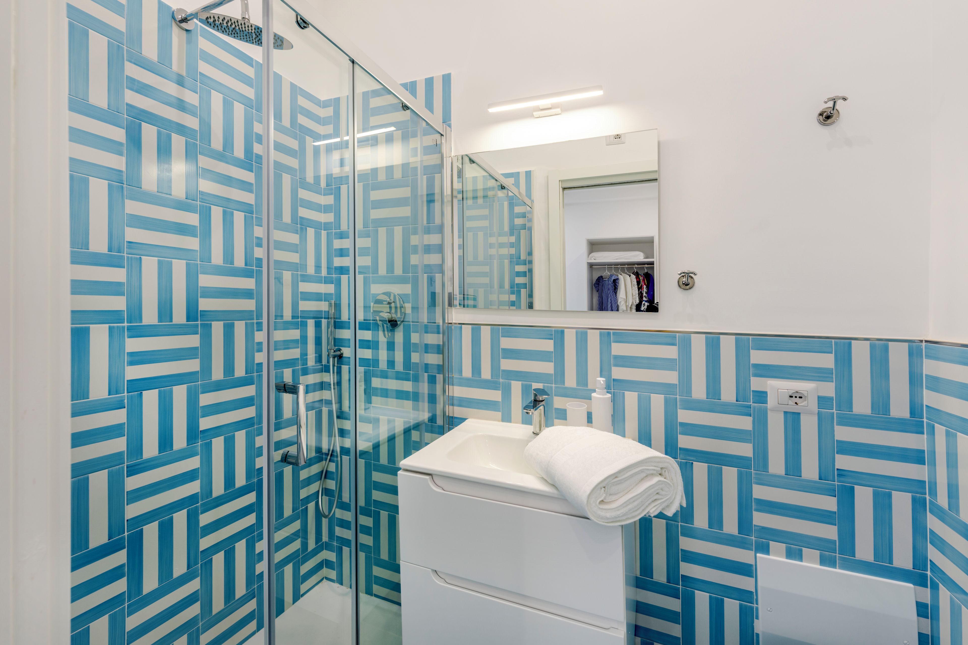 Un baño moderno con cabina de ducha de vidrio, un lavamanos blanco y un espejo sobre el mueble de baño.