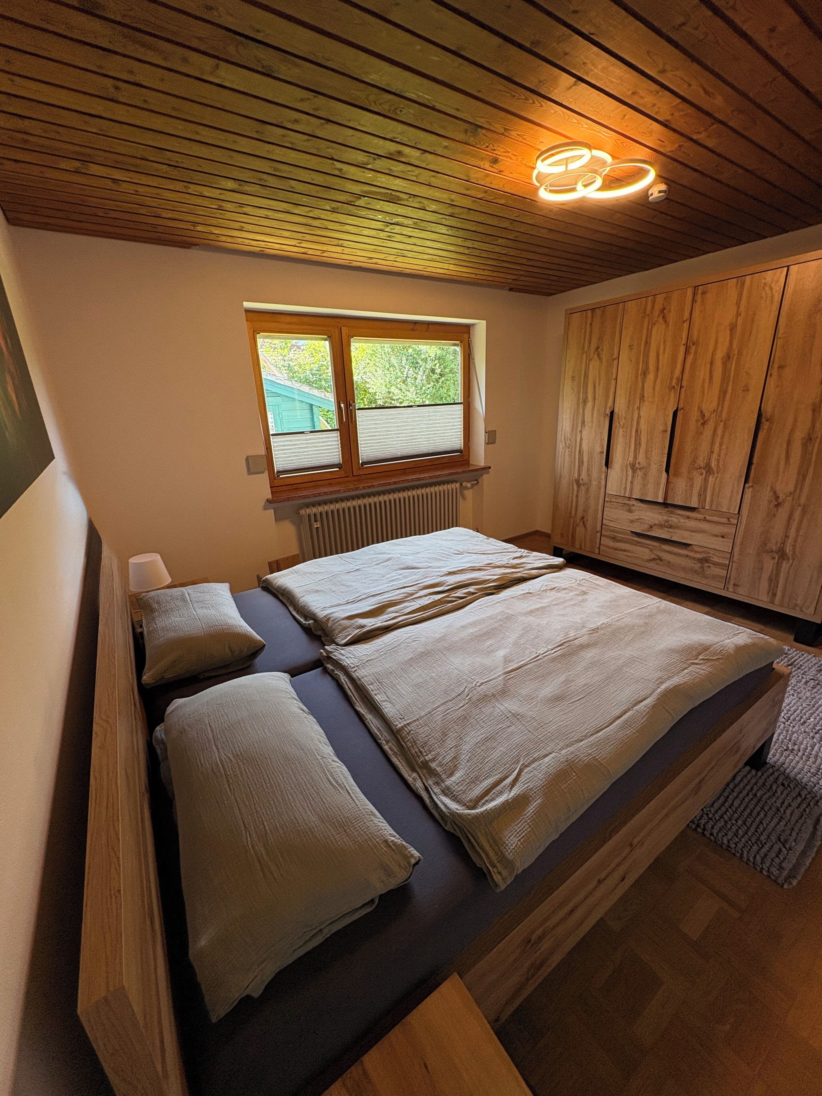 Ein Schlafzimmer mit einem Bett, Holzboden, Fenster mit Jalousien und einer Heizung.