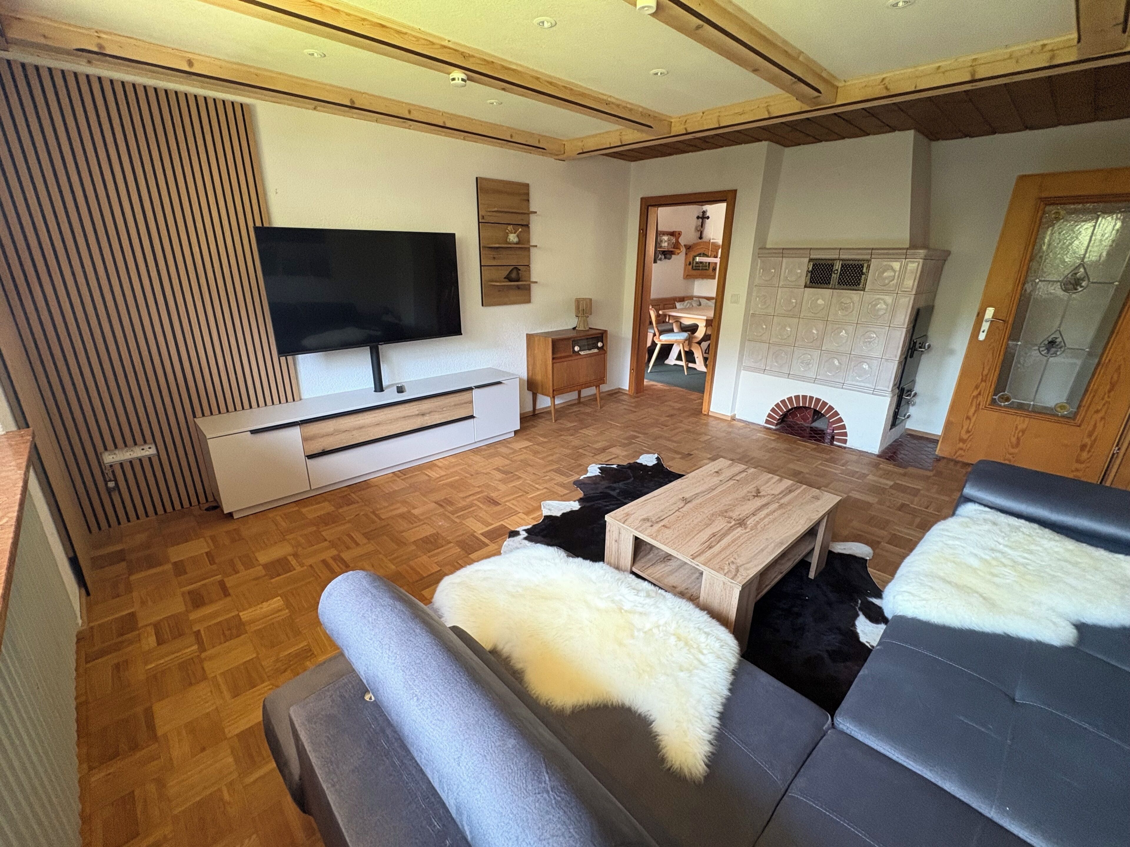 Ein modernes Wohnzimmer mit Flachbildfernseher, Holzboden, einer Couch, einem Couchtisch und einem Kamin.