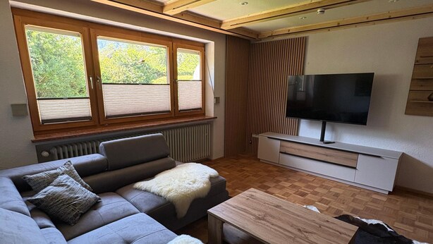 Un salon moderne avec un canapé, une table basse, un téléviseur et une fenêtre équipée de stores.