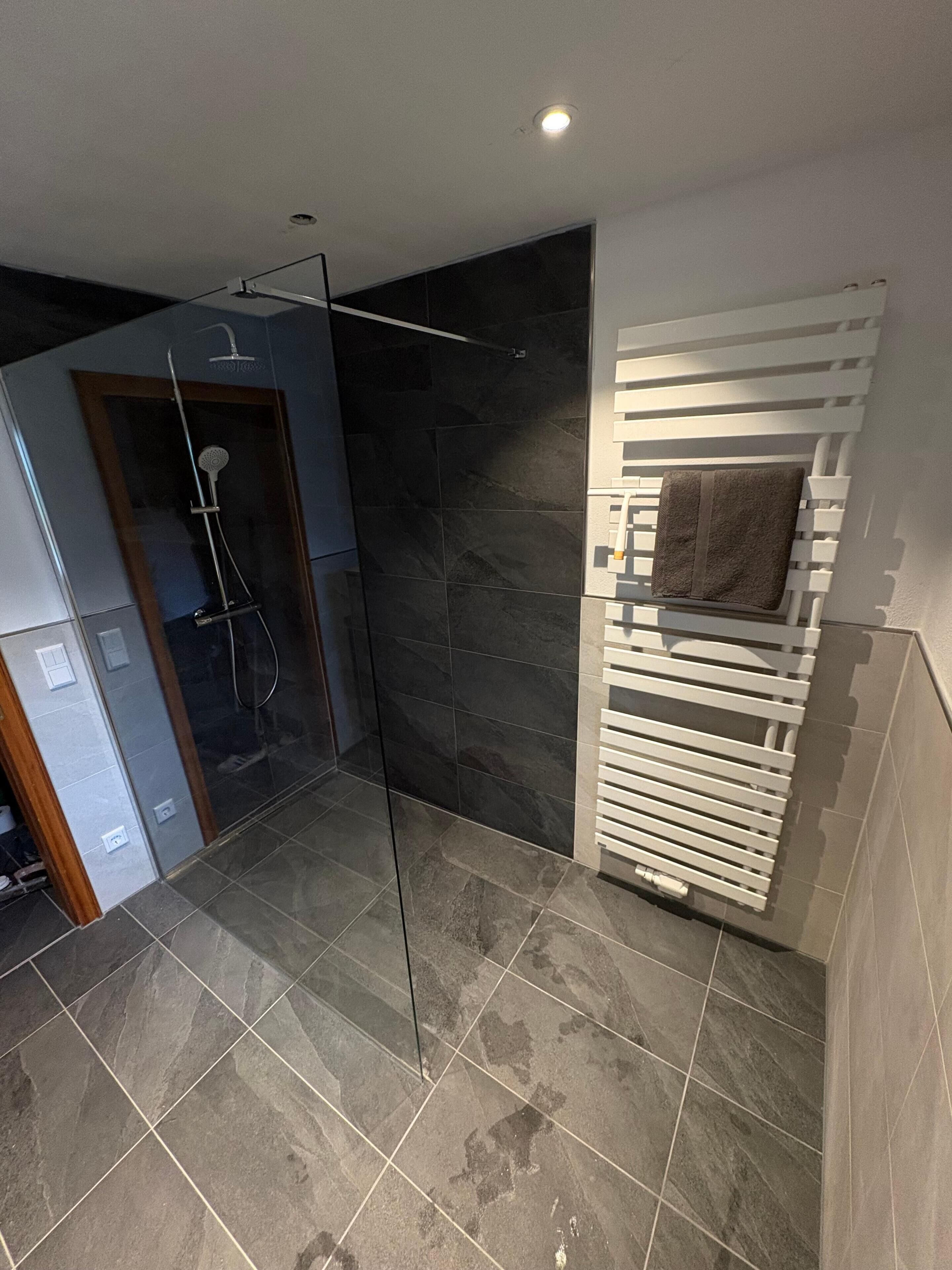 Ein modernes Badezimmer mit Duschabtrennung aus Glas, dunklen Fliesen und einem integrierten Handtuchhalter.