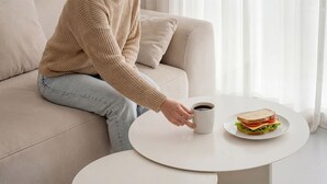 A person sitting on a sofa with a plate of sandwich and a cup of coffee on a small table. - Pohang Baritdol Pension (Pohang)
